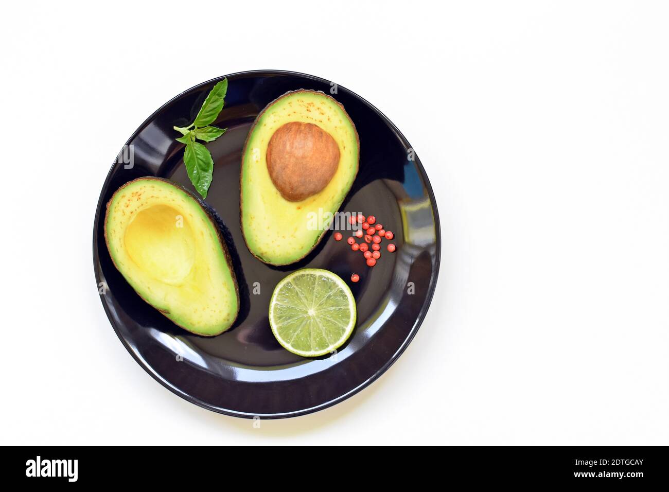 Piatto nero con avocado crudo e una fetta di lime su sfondo bianco. Tabella superiore con testo di copia. Foto Stock