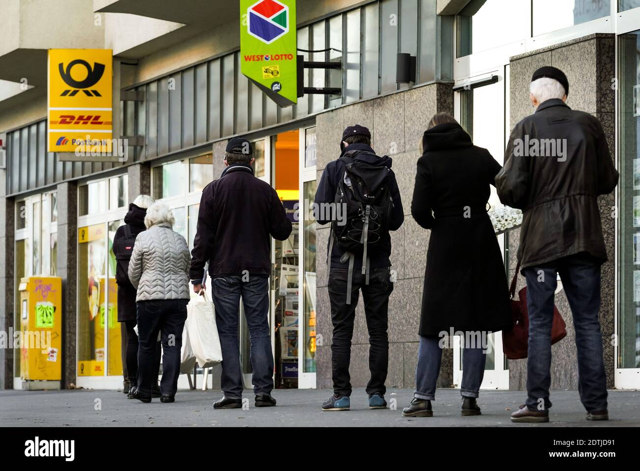Dortmund, Germania, 18 dicembre 2020: I clienti aspettano sul marciapiede di fronte ad una filiale di Deutsche Post/DHL a Dortmund. A causa delle limitazioni del secondo blocco della pandemia corona, solo 3 clienti sono autorizzati a rimanere in questa filiale contemporaneamente. Foto Stock
