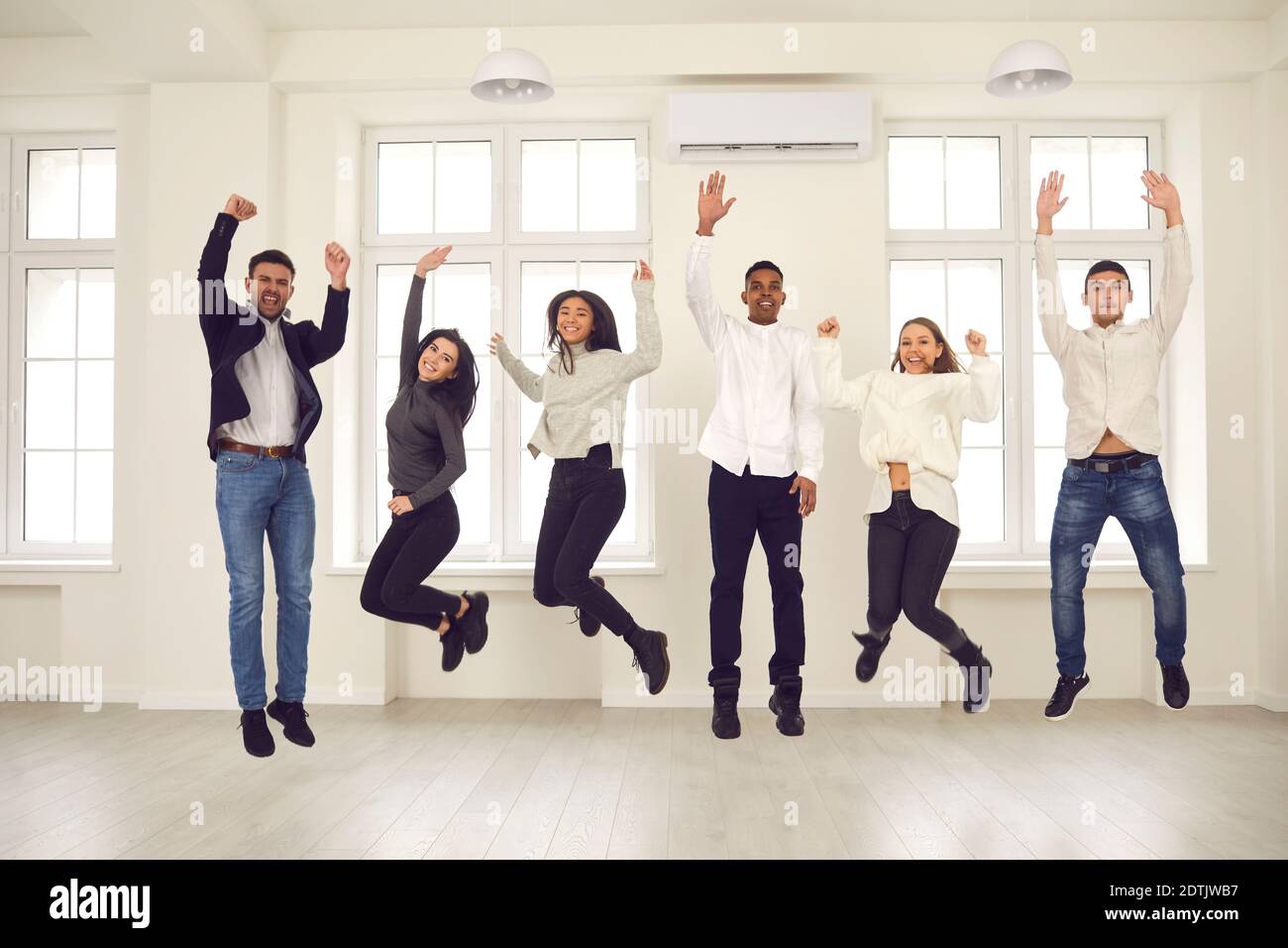 Gruppo di giovani felici che saltano per gioia, celebrando la collaborazione e il successo Foto Stock