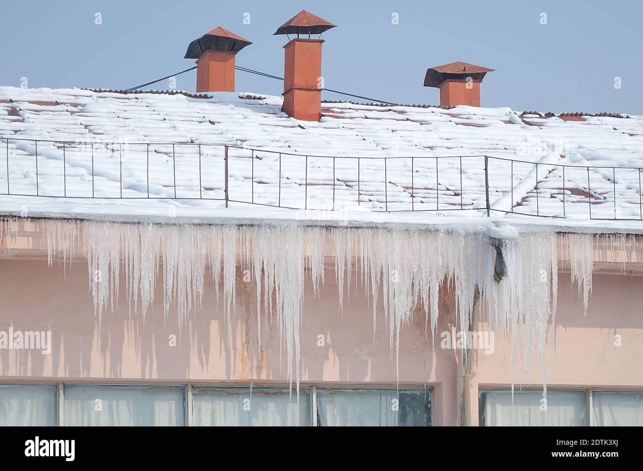 Grandi icicles appendono dal tetto dell'edificio in inverno e c'è neve sul tetto Foto Stock