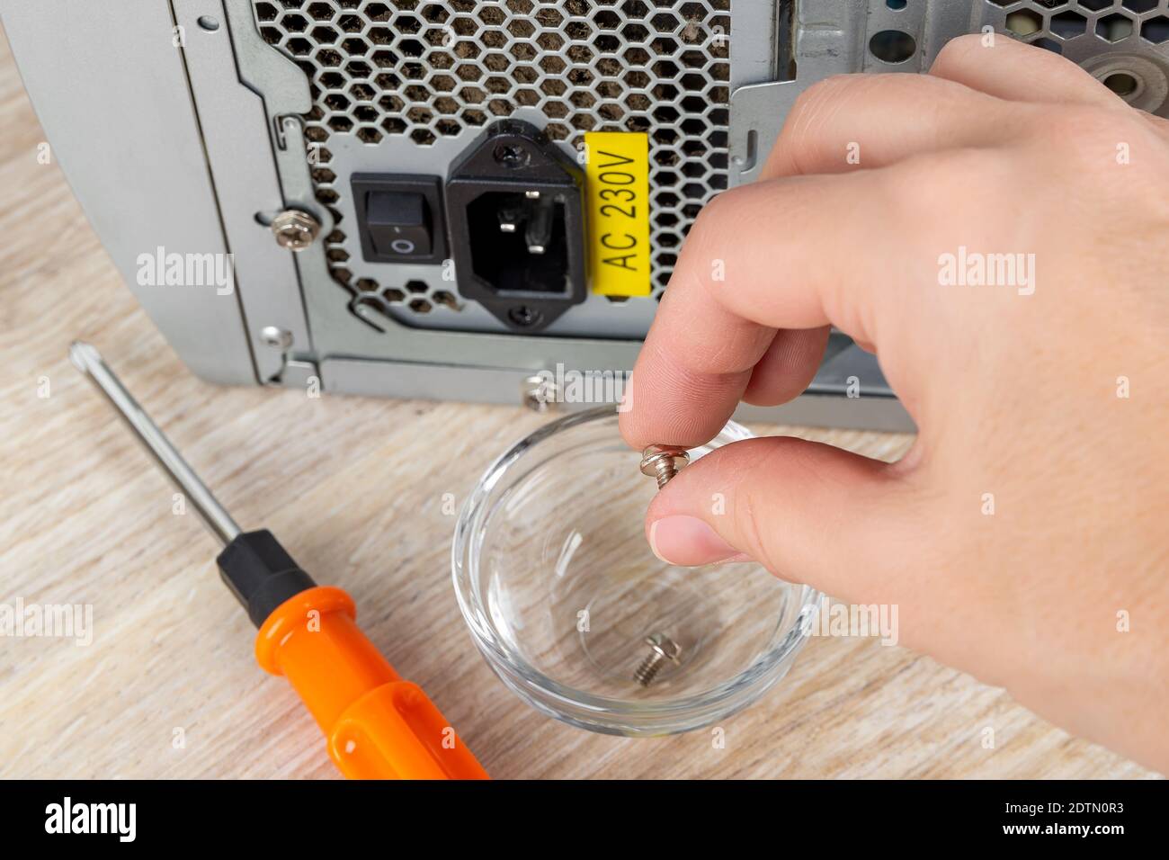 La donna ha rimosso a mano la vite che fissa l'unità di alimentazione nella custodia del pc e la ha ripportata nel recipiente di vetro su una scrivania. Replica PSU del personal computer. Foto Stock