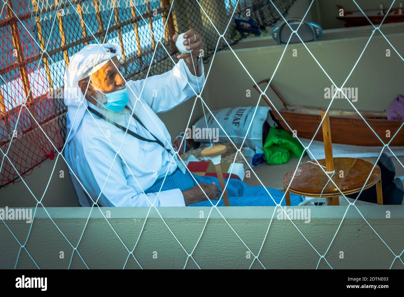 Pescatore arabo, riparando la rete di pesca fatta in casa e yacht di legno, indossando la maschera facciale e si siede sul pavimento del tradizionale boam Foto Stock