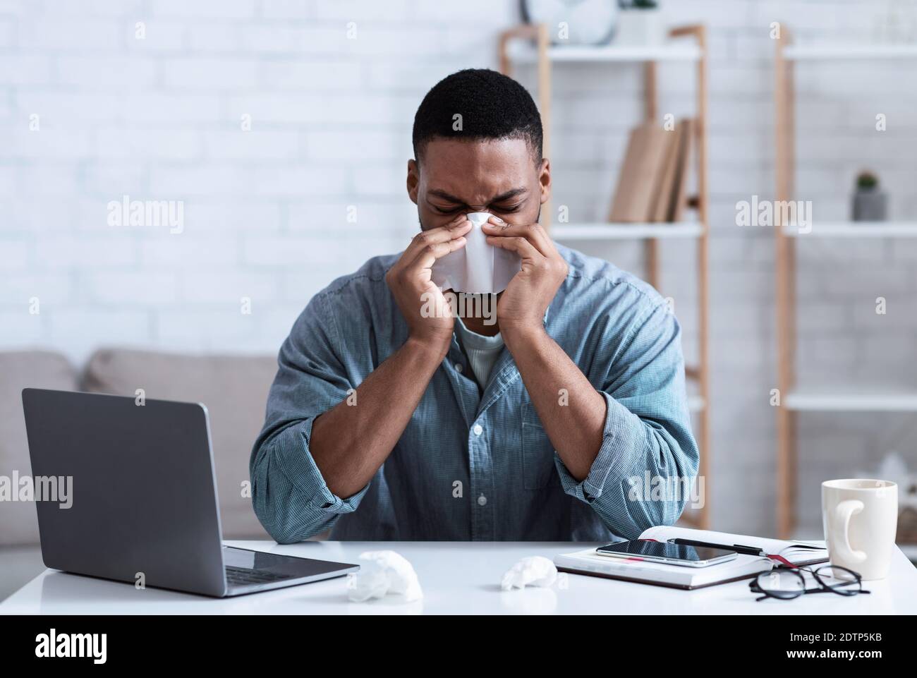 Malato nero Guy soffiando naso in tovagliolo che lavora in ufficio Foto Stock