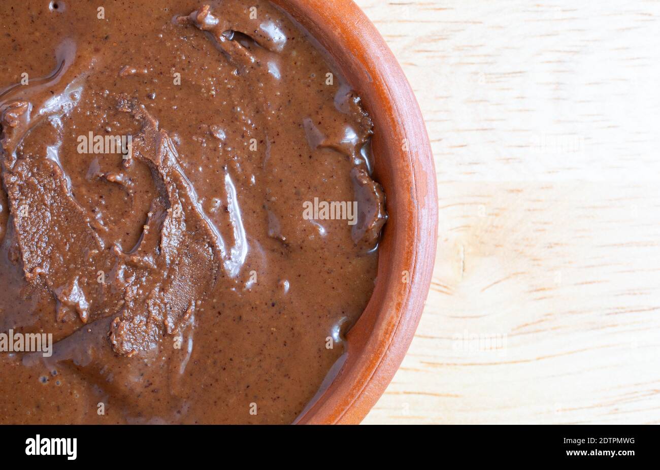 Vista dall'alto di una ciotola di burro di nocciole di mandorle al cioccolato su un tavolo in legno illuminato con luce naturale. Foto Stock