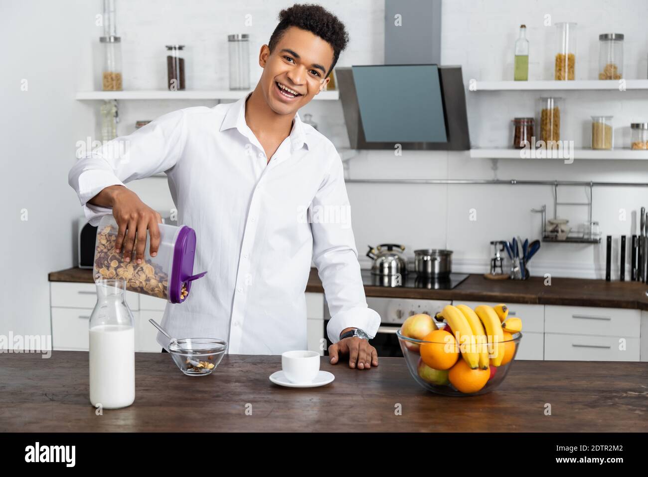 felice afroamericano che prepara la colazione vicino a frutta e bevande sul tavolo Foto Stock