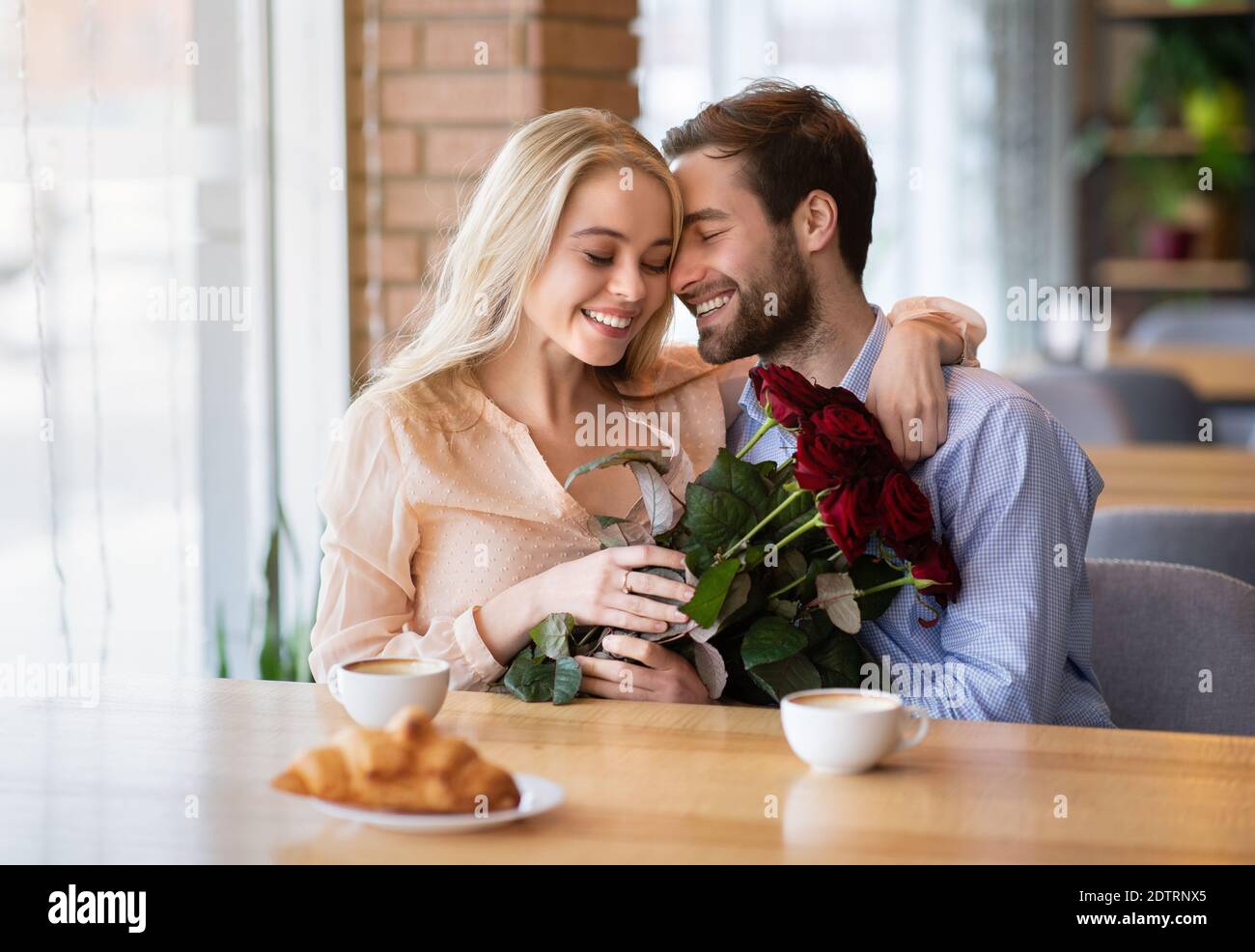 Millennial coppia in hugging di amore e cuddling nel caffè, tenendo bouquet di fiori, celebrando San Valentino Foto Stock