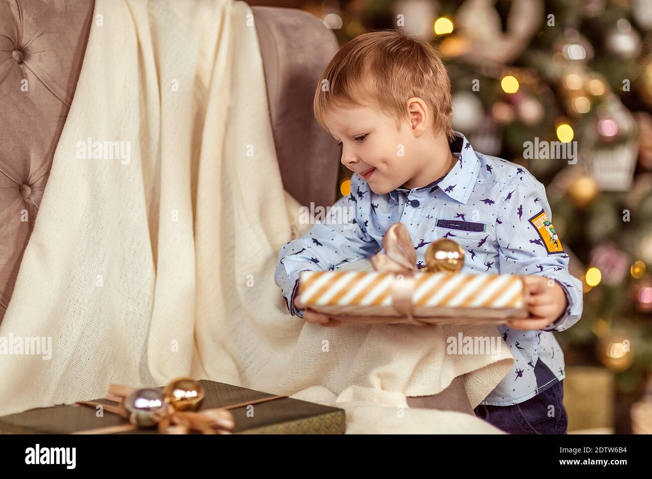 Un bel ragazzo di 4-5 anni si trova vicino al divano e tiene i regali nelle sue mani. Il concetto di vacanze invernali. Messa a fuoco morbida selettiva, bokeh (blurr Foto Stock