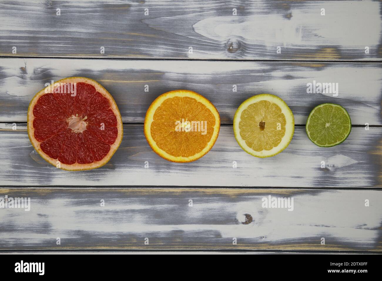 Vista dall'alto su quattro metà isolate di frutta tagliata in fila, pompelmo rosso maturo, arancio, limone giallo e lime verde su tavola di legno bianco naturale con co Foto Stock