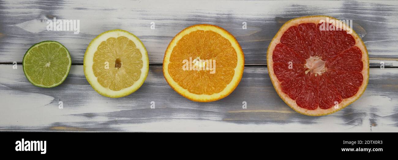 Vista dall'alto su quattro metà isolate di frutta tagliata in fila, pompelmo rosso maturo, arancio, limone giallo e lime verde su tavola di legno bianco naturale con co Foto Stock