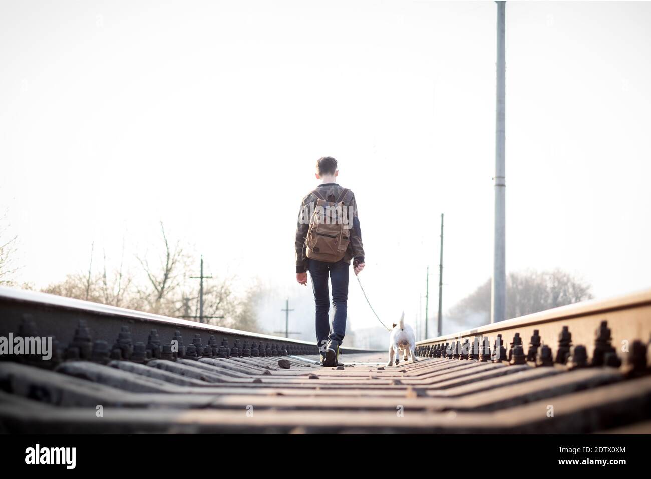 Adolescente su ferrovia a piedi con piccolo cane bianco. La libertà e la solitudine concept Foto Stock