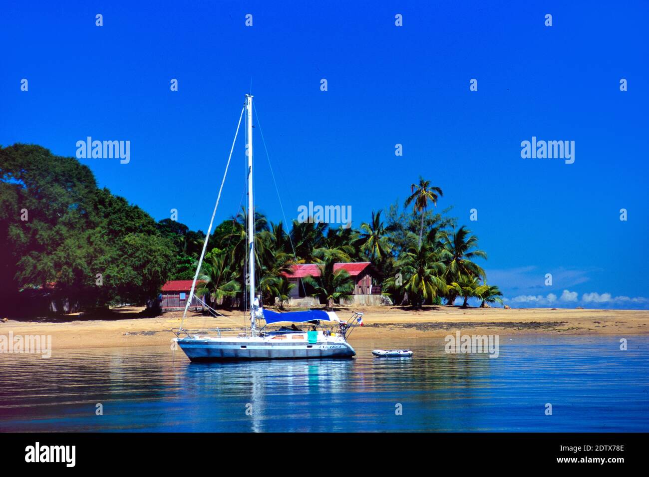 Yacht singolo ormeggiato al largo della spiaggia con le palme a Nosy Komba Isola vicino a Nosy Be Madagascar Foto Stock