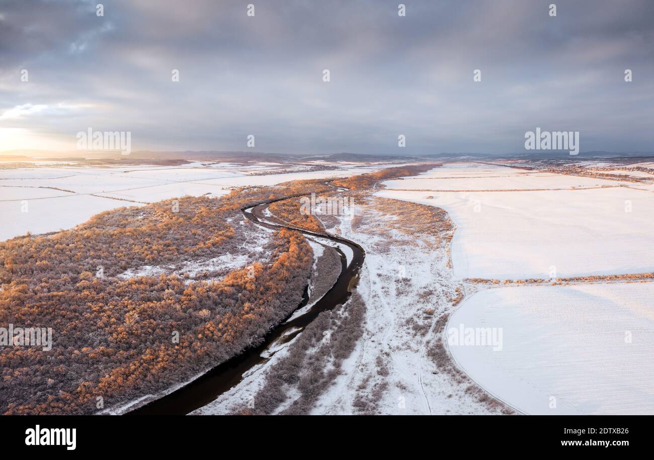 Volo attraverso il maestoso fiume, la foresta ghiacciata e i campi invernali ghiacciati all'alba. Fotografia di paesaggio Foto Stock