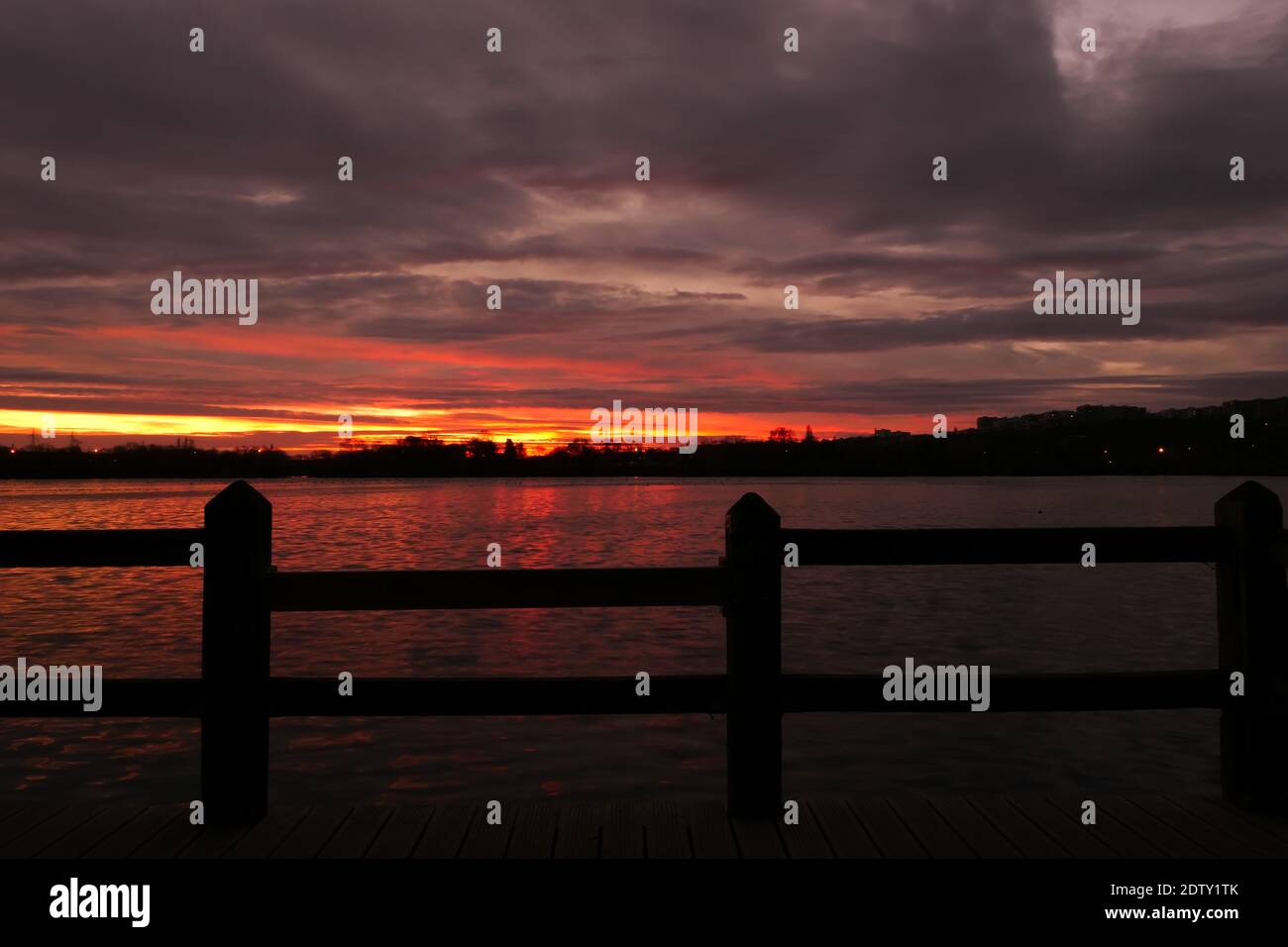 Incredibile alba o tramonto su un lago. Cielo drammatico con nuvole all'orizzonte con acqua e recinzione in legno in primo piano. Foto Stock