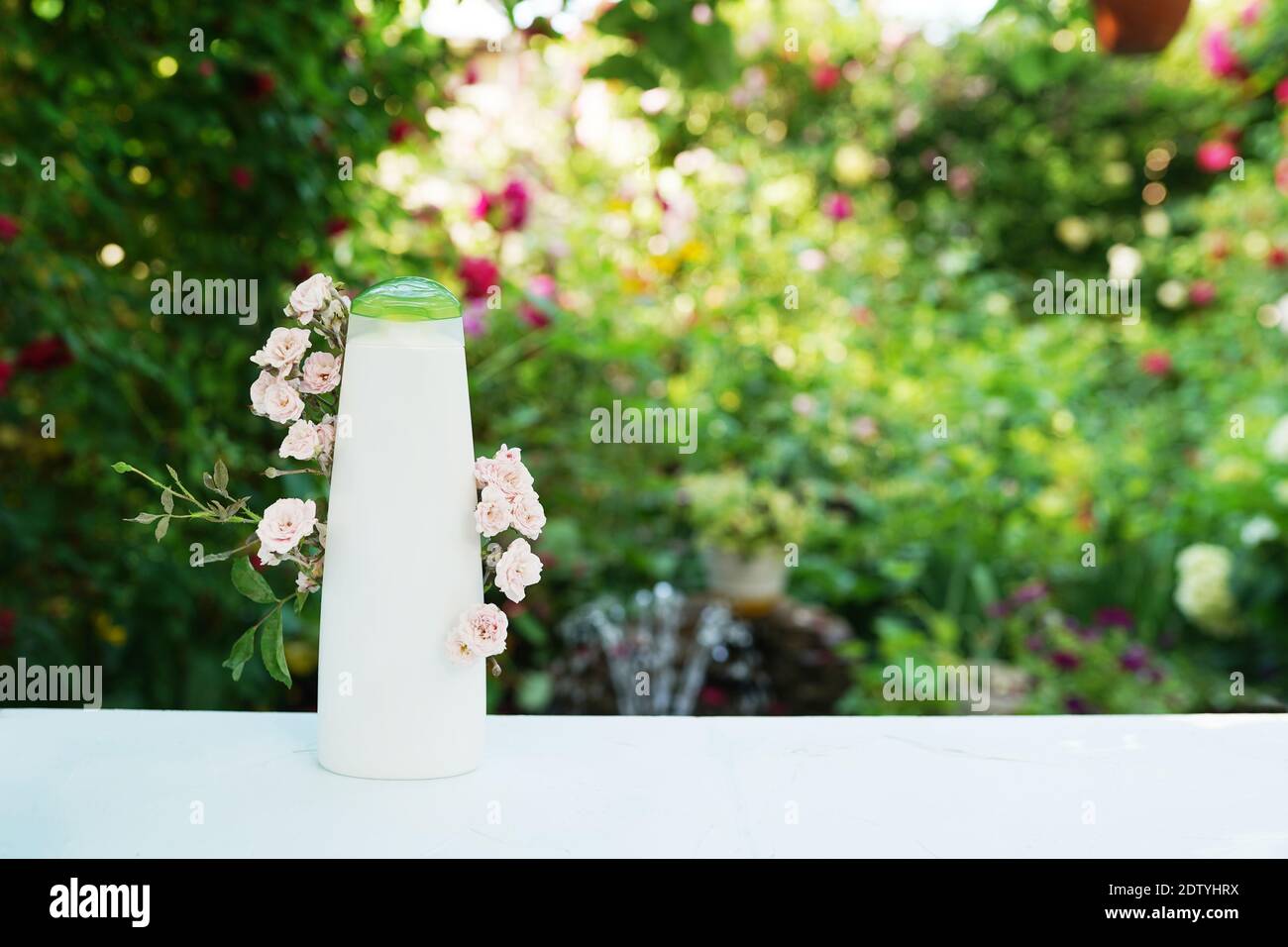 Prodotto per la cura del corpo o dei capelli, shampoo o gel doccia con piccole rose rosa su sfondo naturale Foto Stock