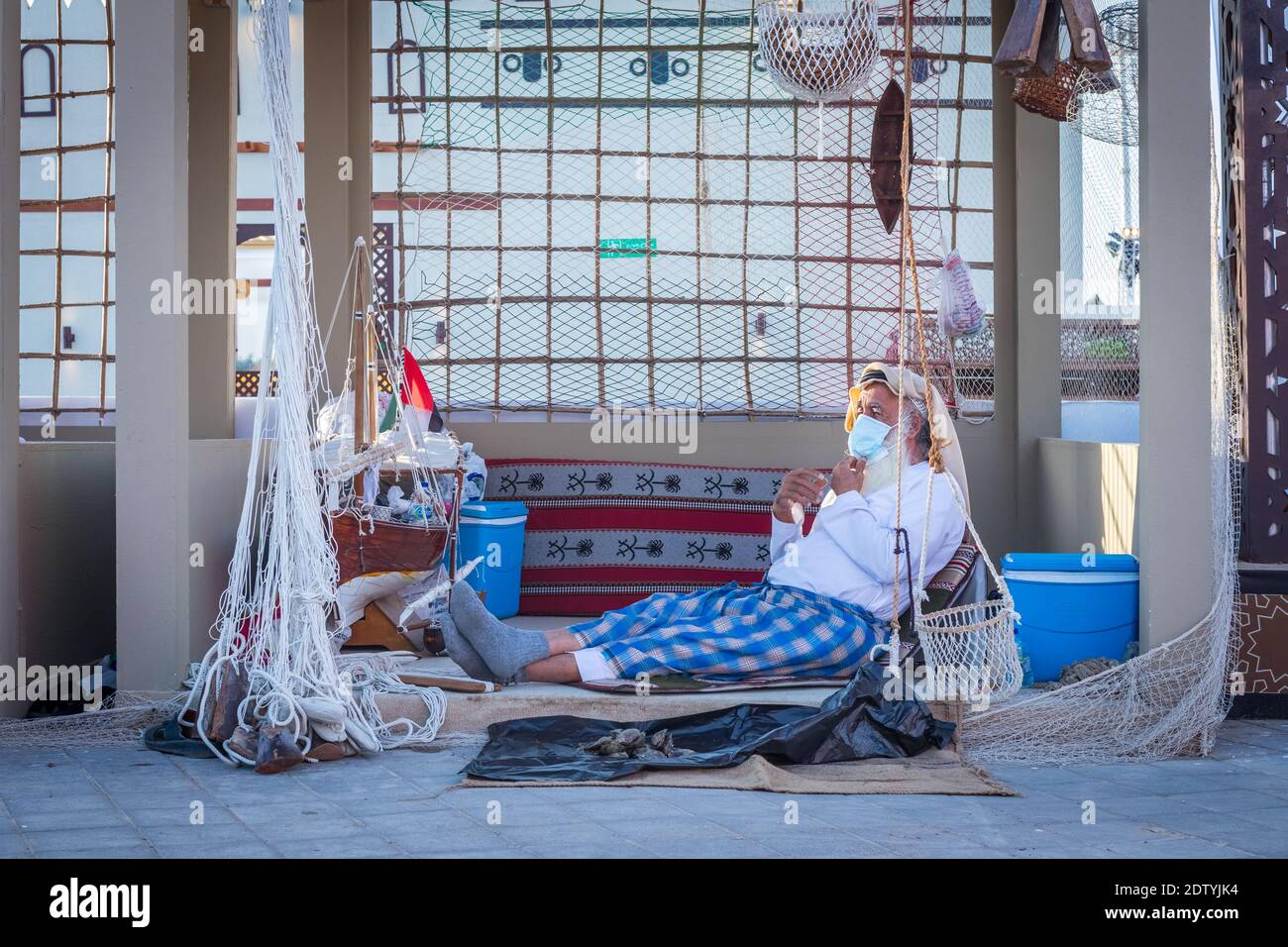 Pescatore arabo, riparando la rete di pesca fatta in casa e yacht di legno, indossando la maschera facciale e si siede sul pavimento del tradizionale boam Foto Stock