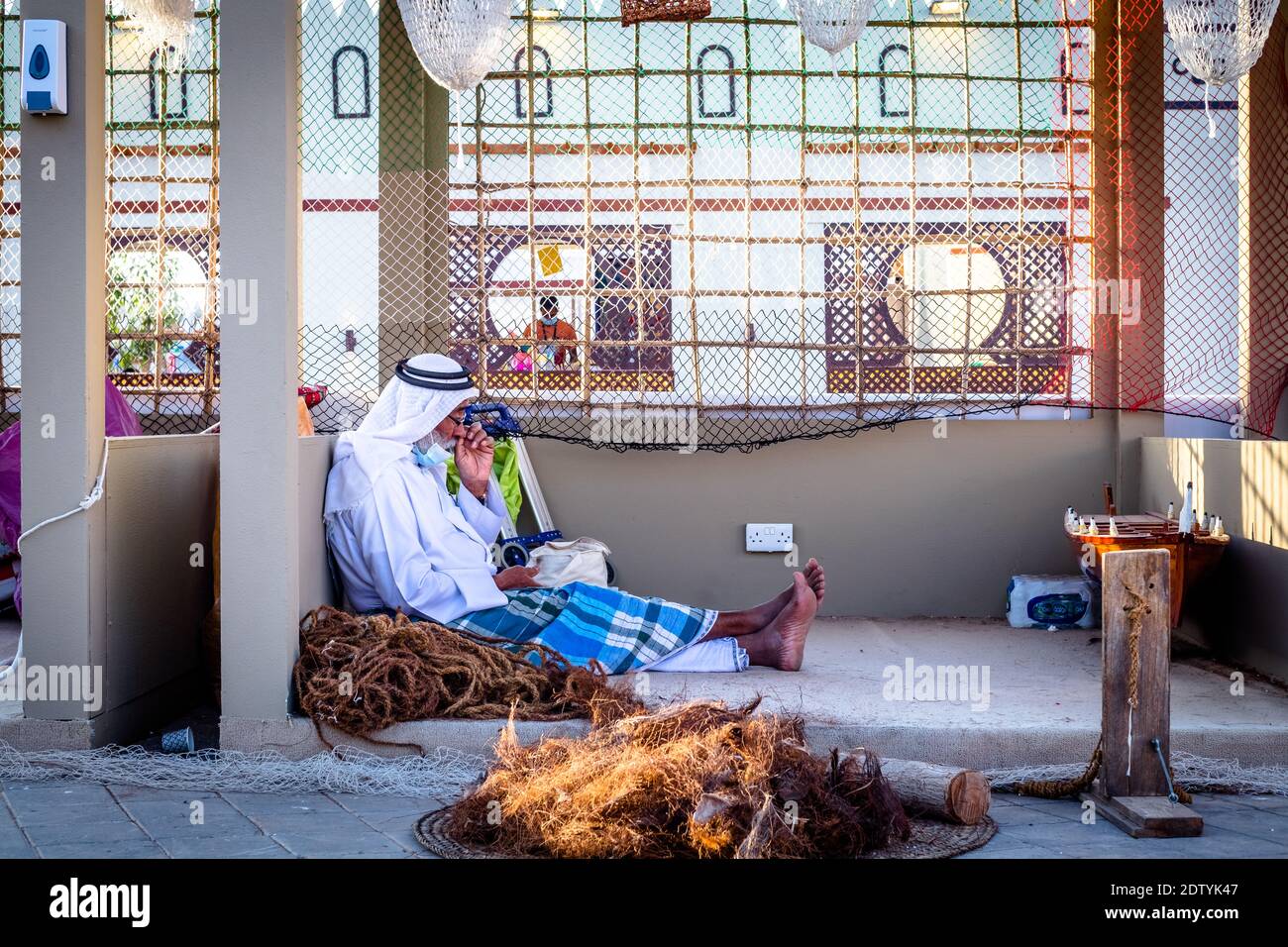 Pescatore arabo, riparando la rete di pesca fatta in casa e yacht di legno, indossando la maschera facciale e si siede sul pavimento del tradizionale boam Foto Stock