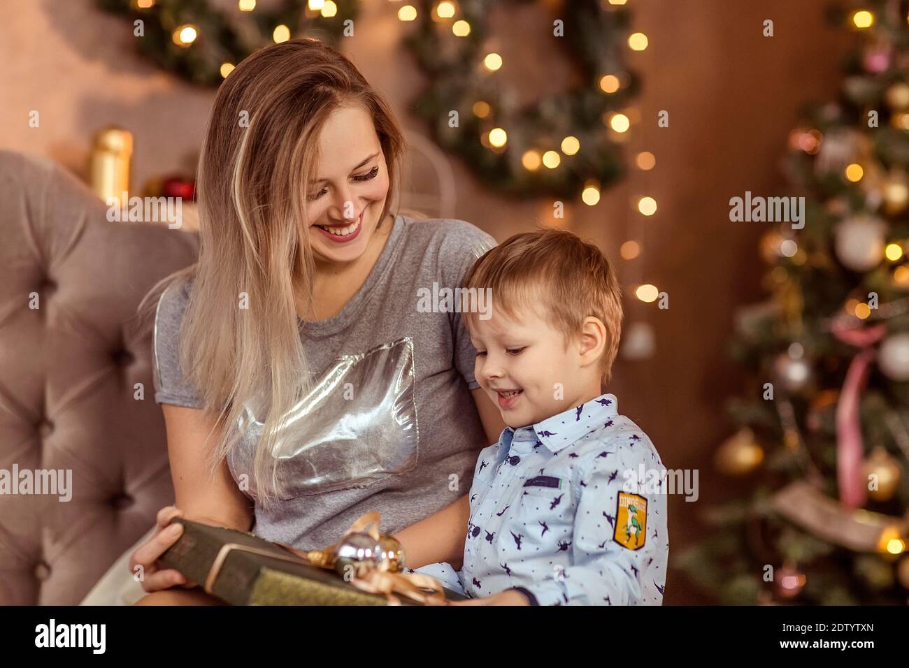 Sorridente giovane ragazza e ragazzo sedersi in una stanza di Natale decorata e godere la vacanza e regali. Messa a fuoco morbida selettiva. Laterale. Il concetto di inverno ho Foto Stock