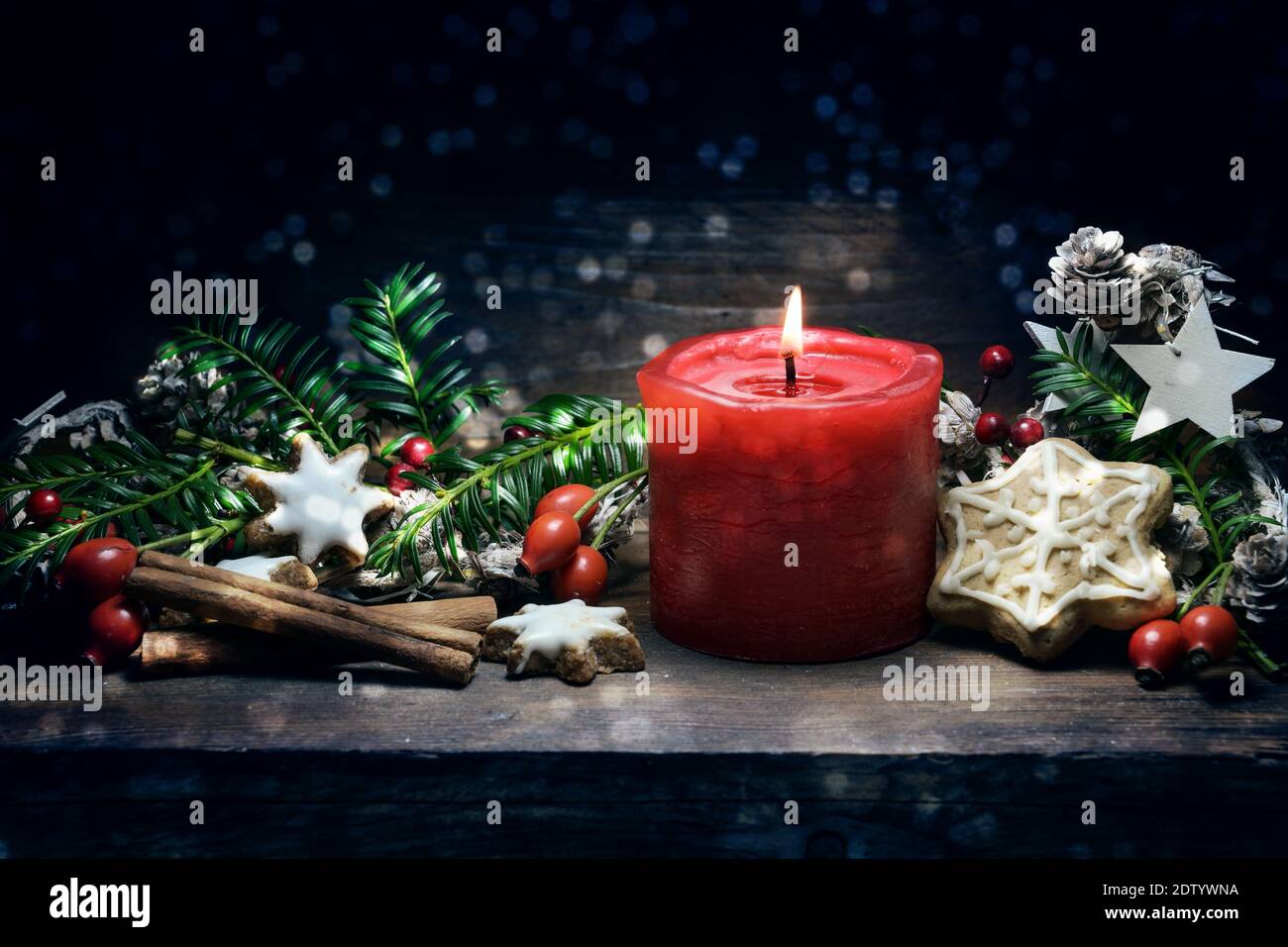 Candela rossa che brucia, biscotti di pan di zenzero, fianchi di rose, rami e coni come decorazione di Natale o di Avvento su uno sfondo di legno blu scuro, spazio di copia, Foto Stock