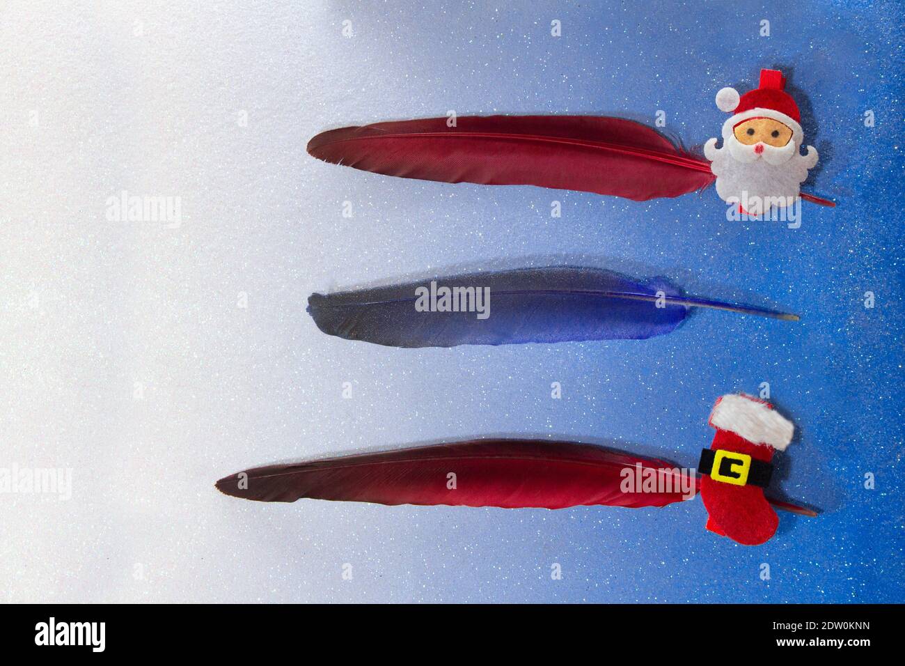 Oro, rosso, blu, piume d'argento con spilla con babbo natale e uno stivale su sfondo blu. Per elenco, scrivere testo, pianificazione. Tre linee. Natale e. Foto Stock