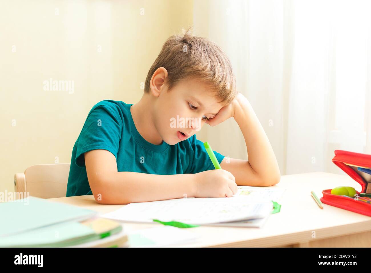 7 sì, vecchio ragazzo seduto alla scrivania e facendo i compiti. I bambini scrivono note nel notebook, compiti difficili, bambini concentrandosi sugli esempi Foto Stock