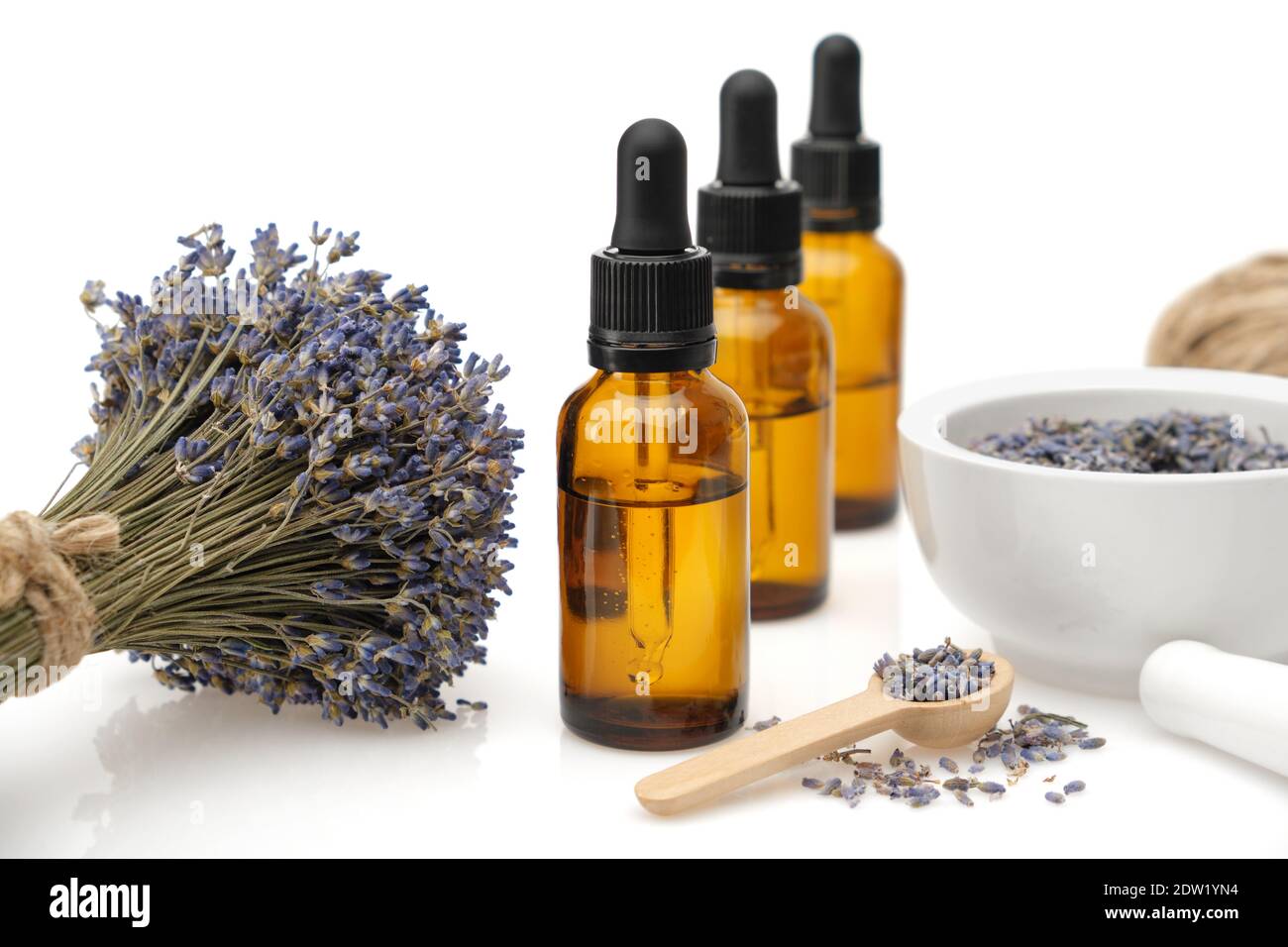 Tre bottiglie di olio essenziale di lavanda o di acqua di fiori aromatici, mortaio e mazzo di fiori di lavanda essiccati su sfondo bianco. Foto Stock