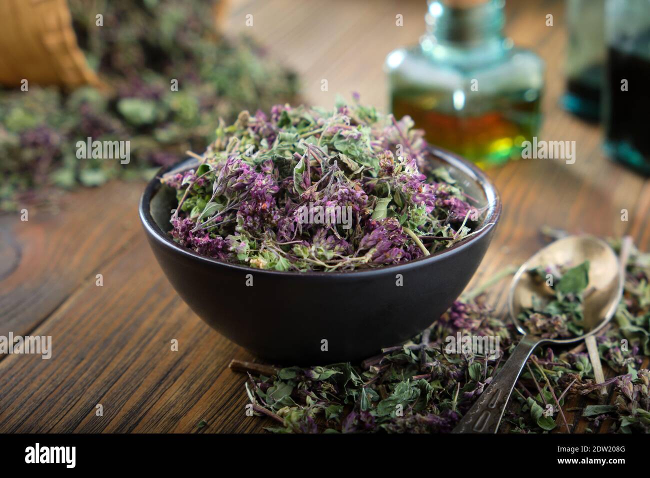 Ciotola di vulgare di origano secco o fiori di maggiorana selvaggi. Bottiglia di olio essenziale sul tavolo. Foto Stock