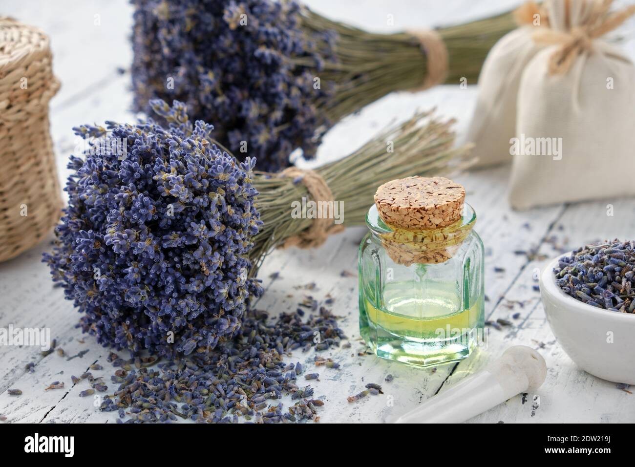 Bottiglia d'olio essenziale alla lavanda, mortaio, bustine e bouquet di fiori secchi alla lavanda. Foto Stock
