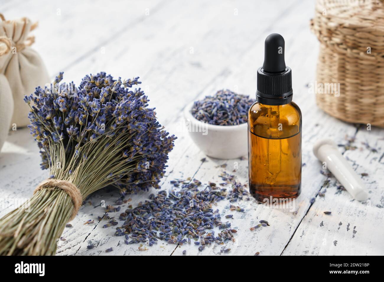 Flacone contagocce di olio essenziale di lavanda, sacchetti e bouquet di fiori di lavanda essiccati su tavolo di legno bianco. Foto Stock