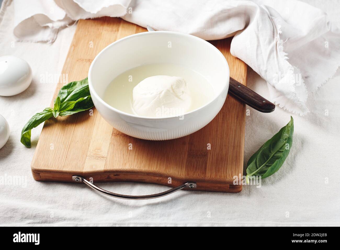 Palla di mozzarella in un recipiente e foglie di basilico fresco. Foto Stock