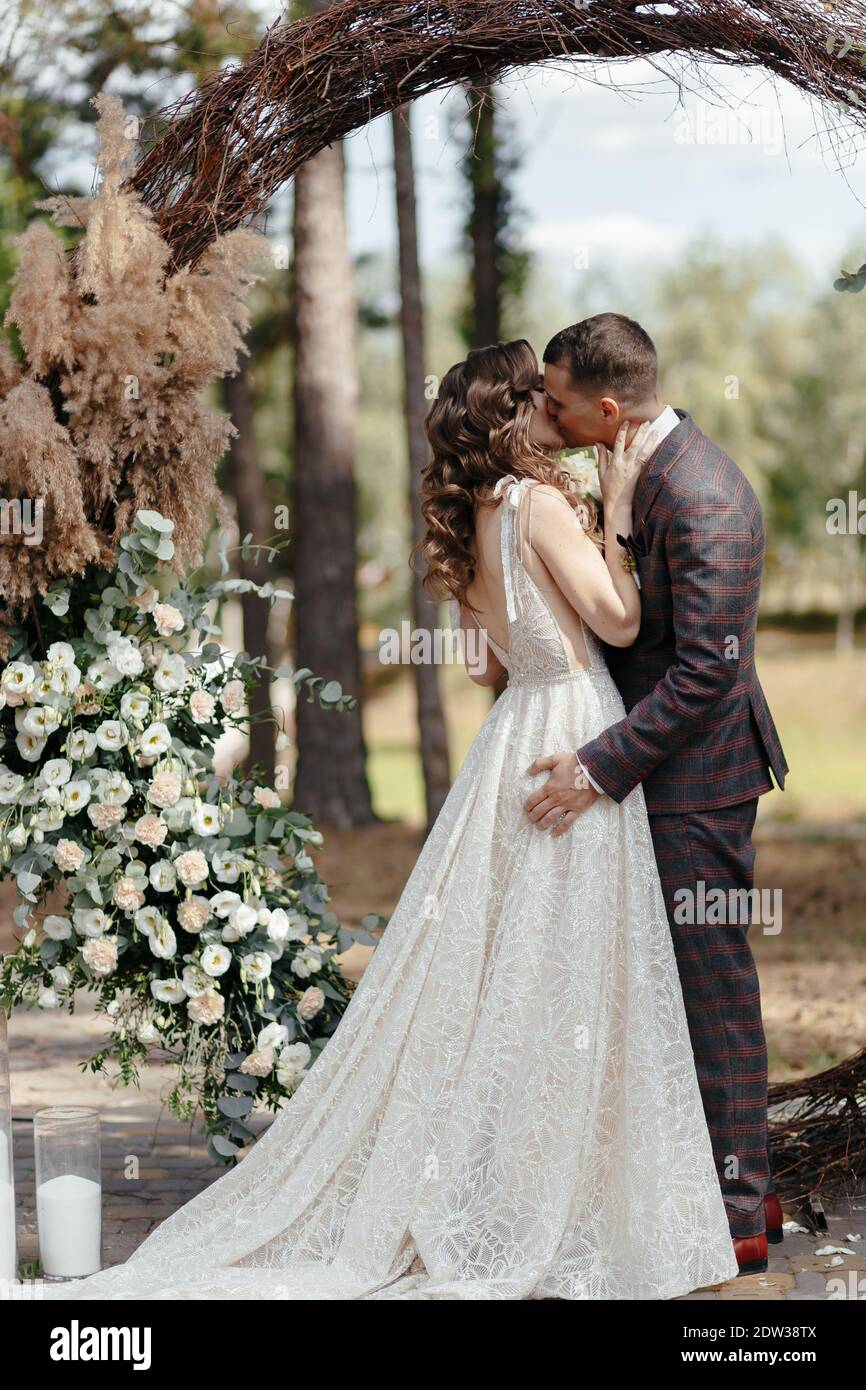 Bride baciante e sposo in piedi davanti all'arco alla cerimonia nuziale. Sposi felici alla cerimonia nuziale Foto Stock