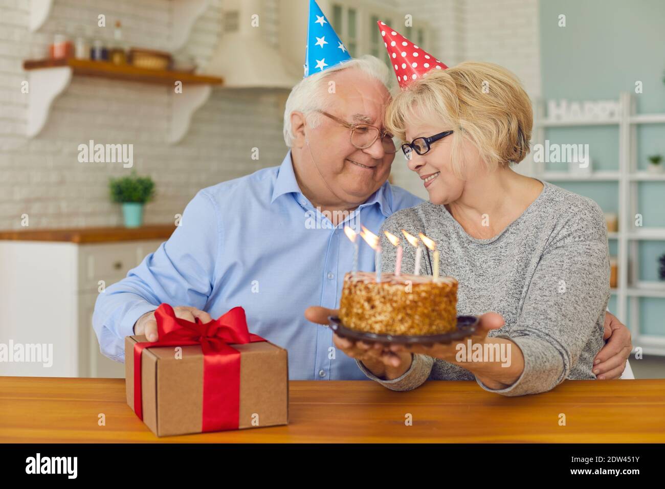 Sorridente coppia senior seduta con torta di compleanno e scatola regalo e guardarsi l'un l'altro Foto Stock