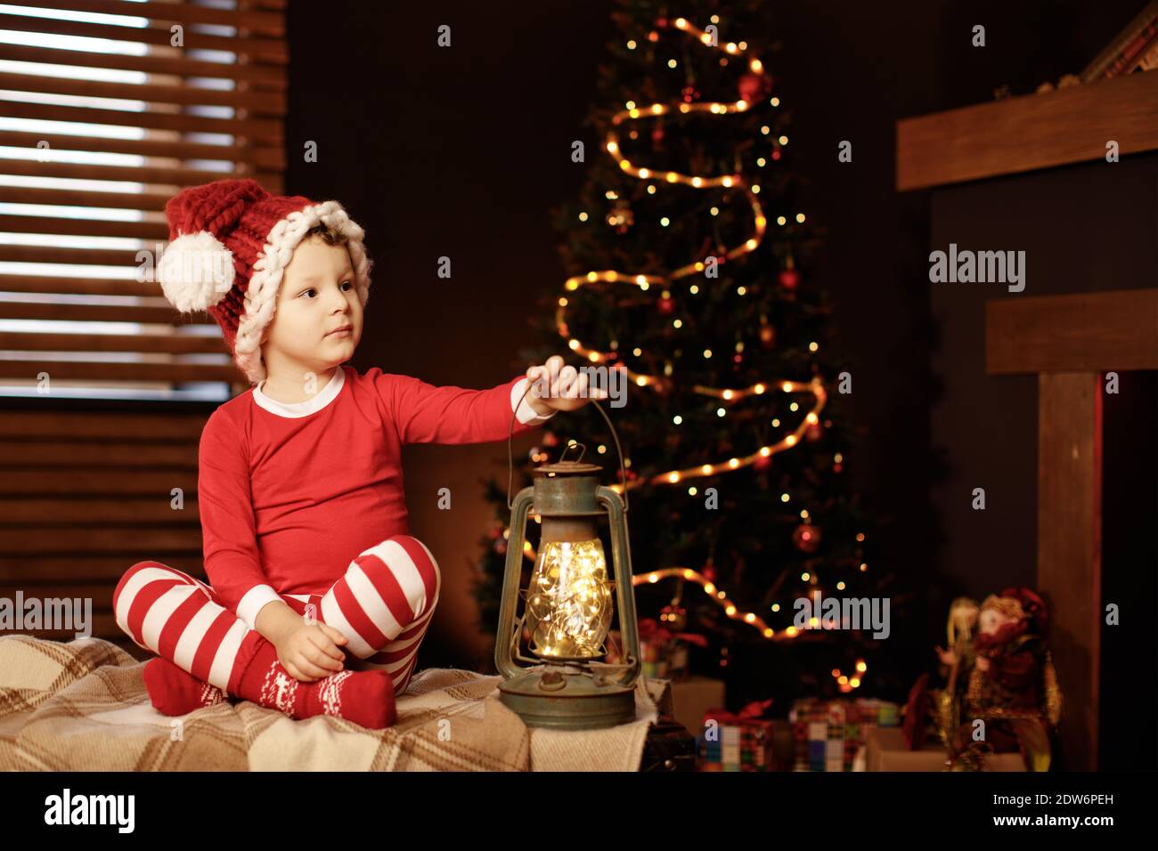 Buon Natale e buone feste UN ragazzino è seduto con una lanterna all'albero di Natale nuovo anno, elfo Foto Stock