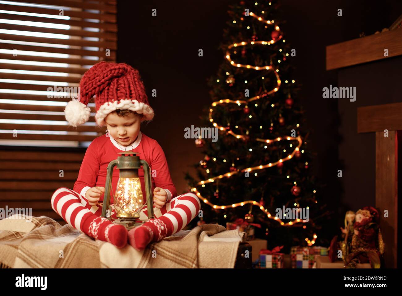 Buon Natale e buone feste UN ragazzino è seduto con una lanterna all'albero di Natale nuovo anno, elfo Foto Stock