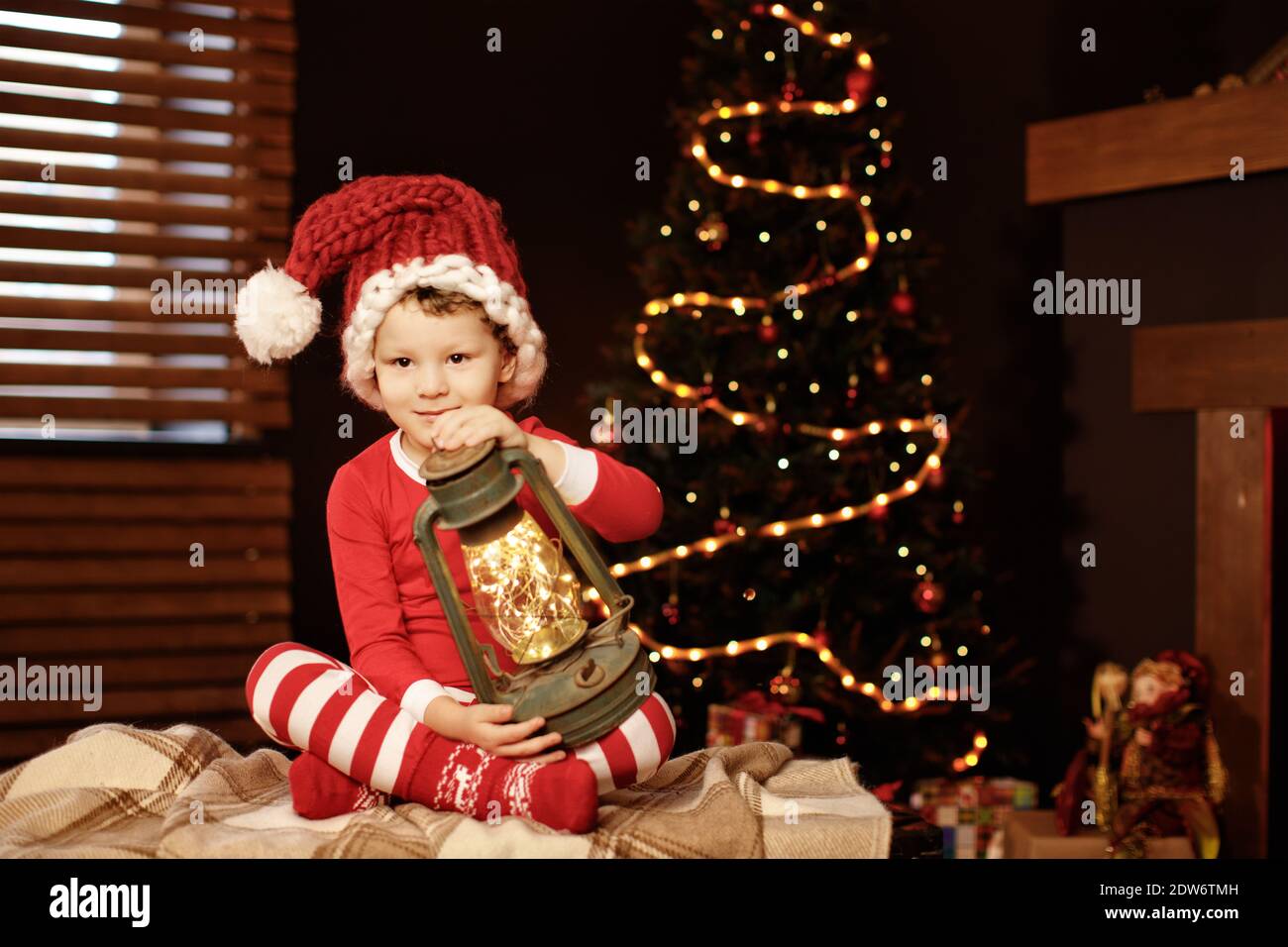 Buon Natale e buone feste UN ragazzino è seduto con una lanterna all'albero di Natale nuovo anno, elfo Foto Stock