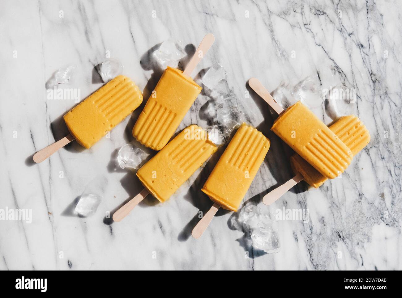 Pop-smoothie vegan gelato al Mango. Piatto-lay di papsicli di frutta di mango su sfondo di marmo grigio sotto la luce del sole, vista dall'alto. Estate desse sano Foto Stock