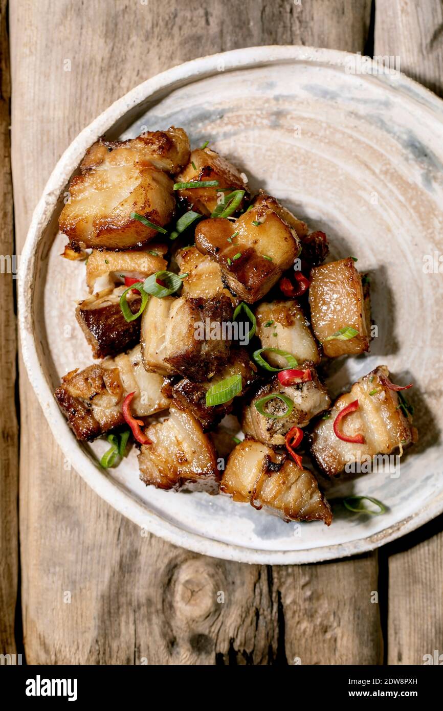 Pancia di maiale fritta alla griglia con peperoncino e cipolla primaverile su piatto di ceramica con bastoncini sopra il vecchio fondo di legno. Disposizione piatta, spazio di copia Foto Stock
