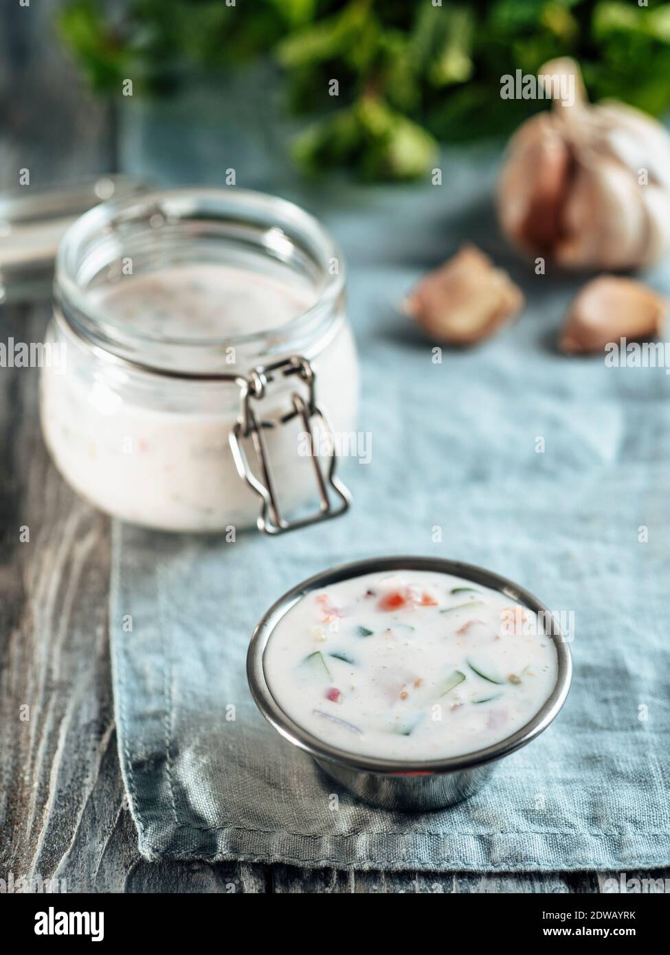 Autentica salsa raita di cetrioli pakistani su tovagliolo di lino blu su sfondo grigio di legno. Salsa di raita immergere con cetrioli, cipolla e pomodori in aggiunta Foto Stock