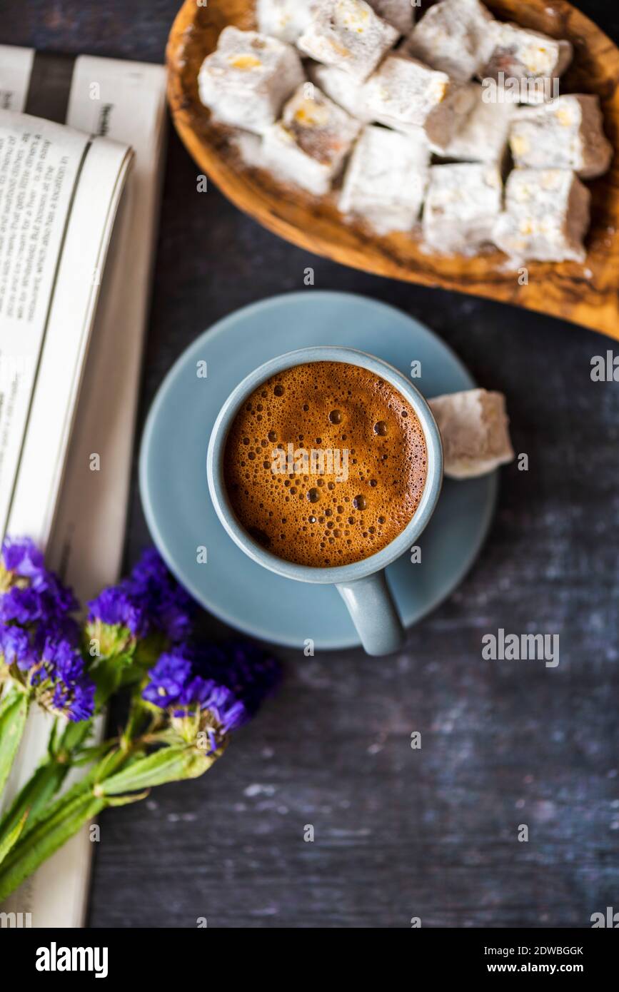 Caffè turco servito in una tazza di caffè grigio e accompagnato da delizie turche, fiori selvatici e giornale su sfondo scuro. Foto Stock