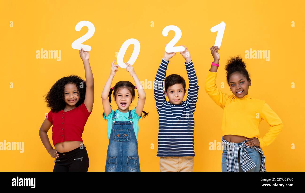 Sorridente simpatico simpatico misto razza bambini in possesso di 2021 numeri isolati su sfondo giallo per i concetti di nuovo anno Foto Stock