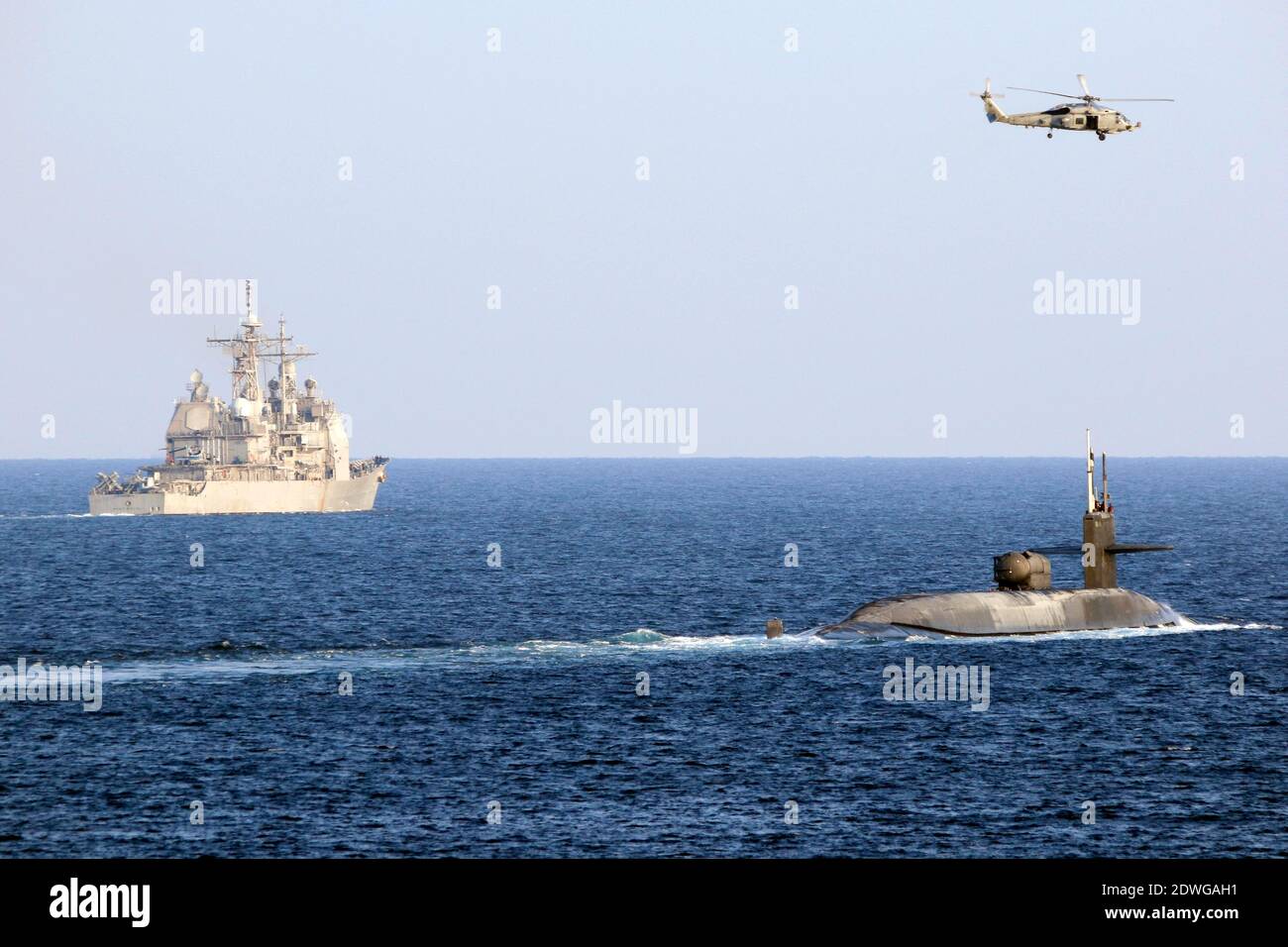 Handout foto datata 21 dicembre 2020 dell'elicottero MH-60R Seahawk, attaccato allo Squadrone Elicopter Sea Maritime (HSM 48), vola sopra il sottomarino missile guidato USS Georgia (SSGN 729) come il sottomarino che transita con l'incrociatore missilistico guidato USS Port Royal di classe Ticonderoga (CG 73) Sullo stretto di HormuzLa Marina statunitense sembra inviare un messaggio in Iran sotto forma di sottomarino missilistico guidato dotato di tremende forze d'artificio e forse di truppe speciali. Il sottomarino missilistico guidato USS Georgia di classe Ohio ha navigato nel Golfo Persico lunedì. Per la prima volta in Foto Stock