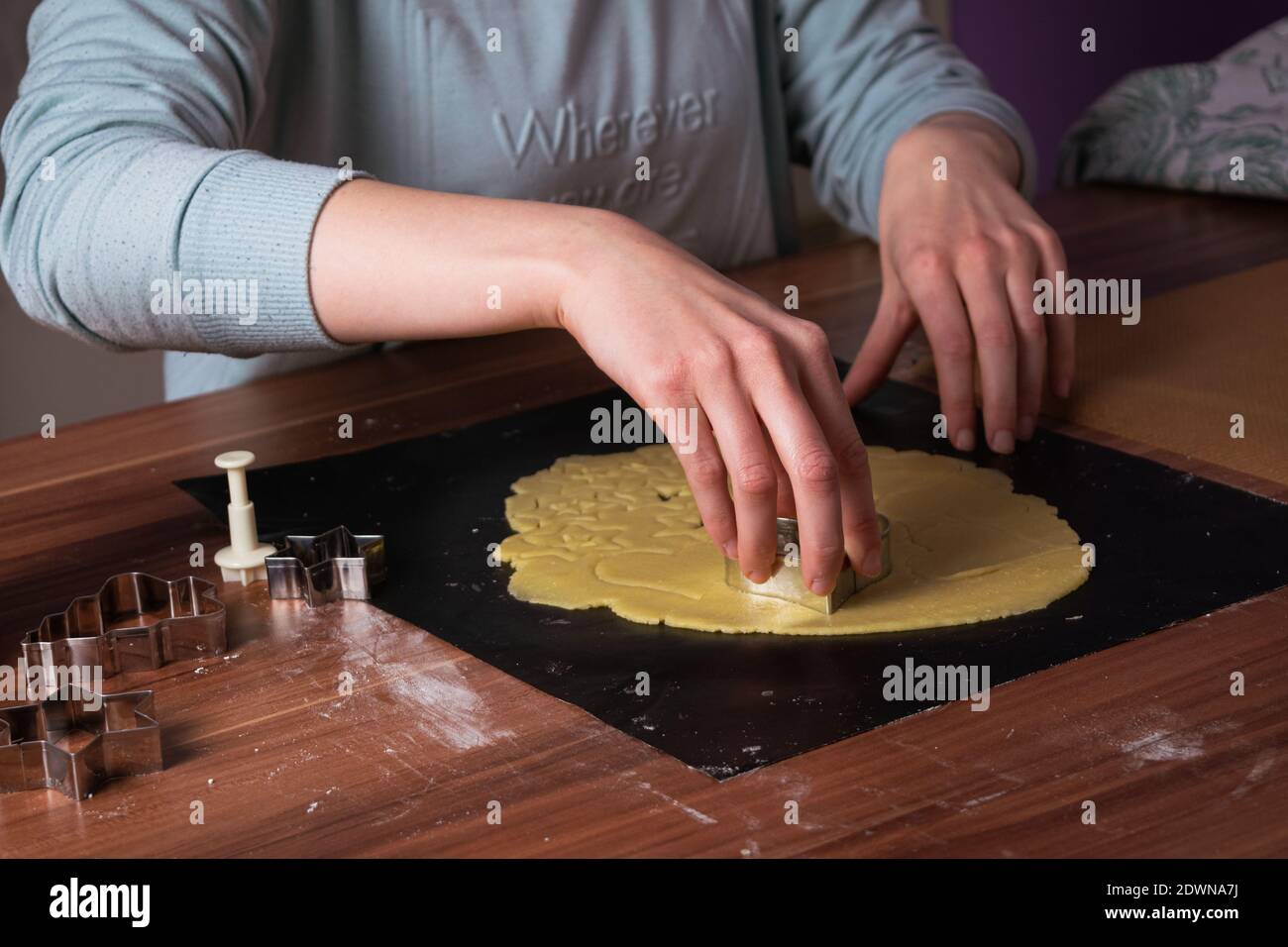 Giovane donna che prepara i biscotti di natale su carta da forno nera sopra tabella Foto Stock