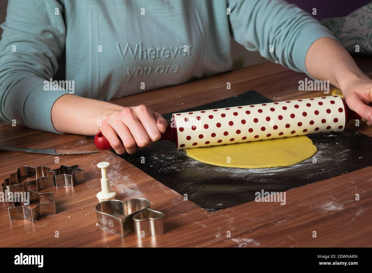 Donna che fa i biscotti di natale su carta da forno nera sul tavolo con rullo per impasto Foto Stock