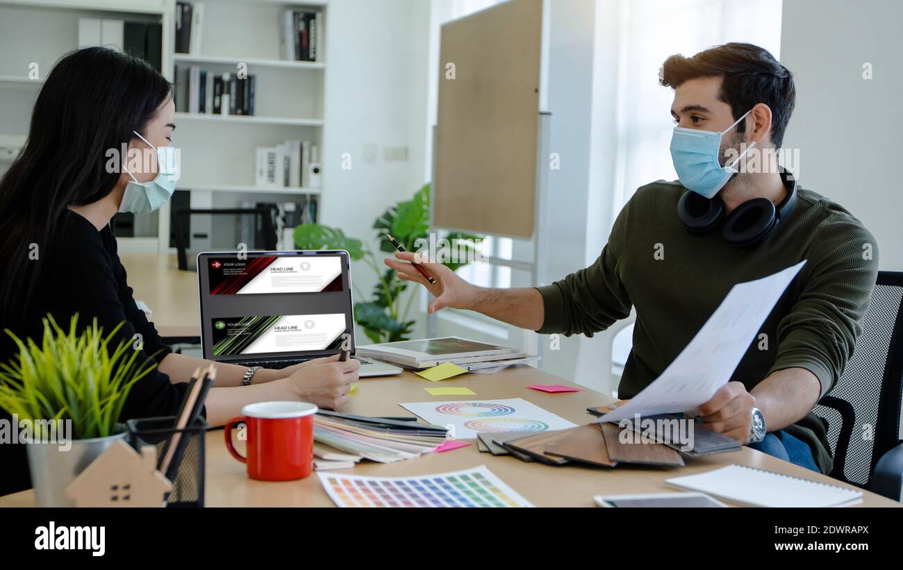 persone creative e designer grafico indossare maschera per proteggere covid 19 o coronavirus, parlare e planare a scegliere il colore per la copertina del libro in ufficio Foto Stock