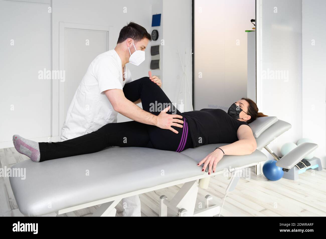 Donna sdraiata sul tavolo da massaggio mentre il suo terapeuta fisico fa esercizi speciali per la terapia fisica per sciatica e problemi nervosi schiacciati. Foto di alta qualità Foto Stock