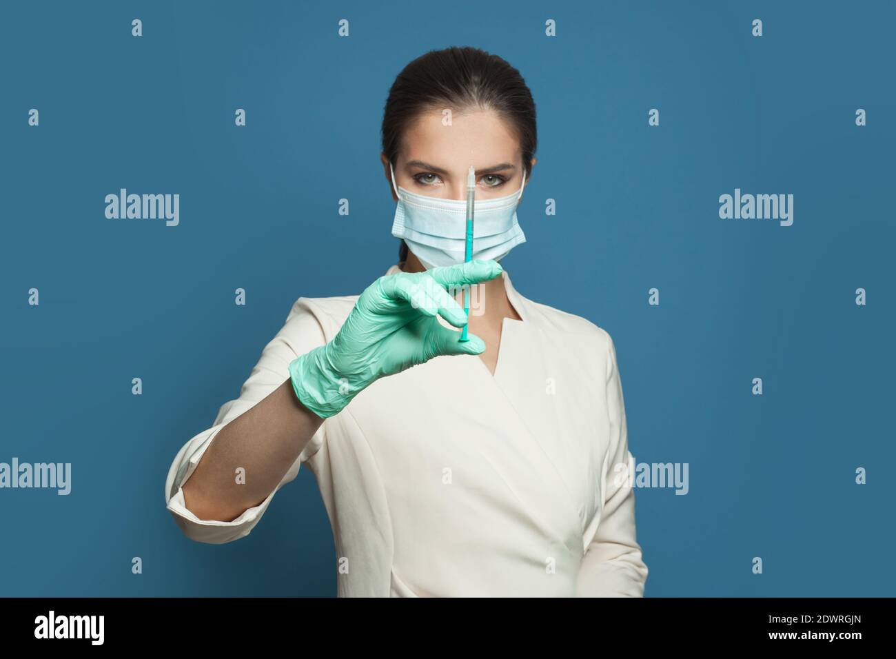 Donna medico o infermiere in maschera medica protettiva che tiene la siringa su sfondo blu. Concetto di medicina, sicurezza e vaccinazione Foto Stock