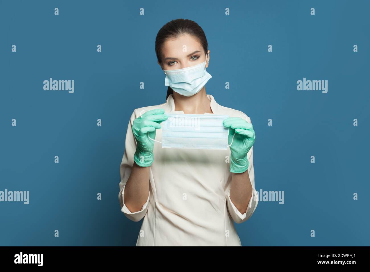 Medico donna o specialista medico che indossa uniforme medica professionale e. maschera protettiva che tiene la maschera medica protettiva su blu Foto Stock