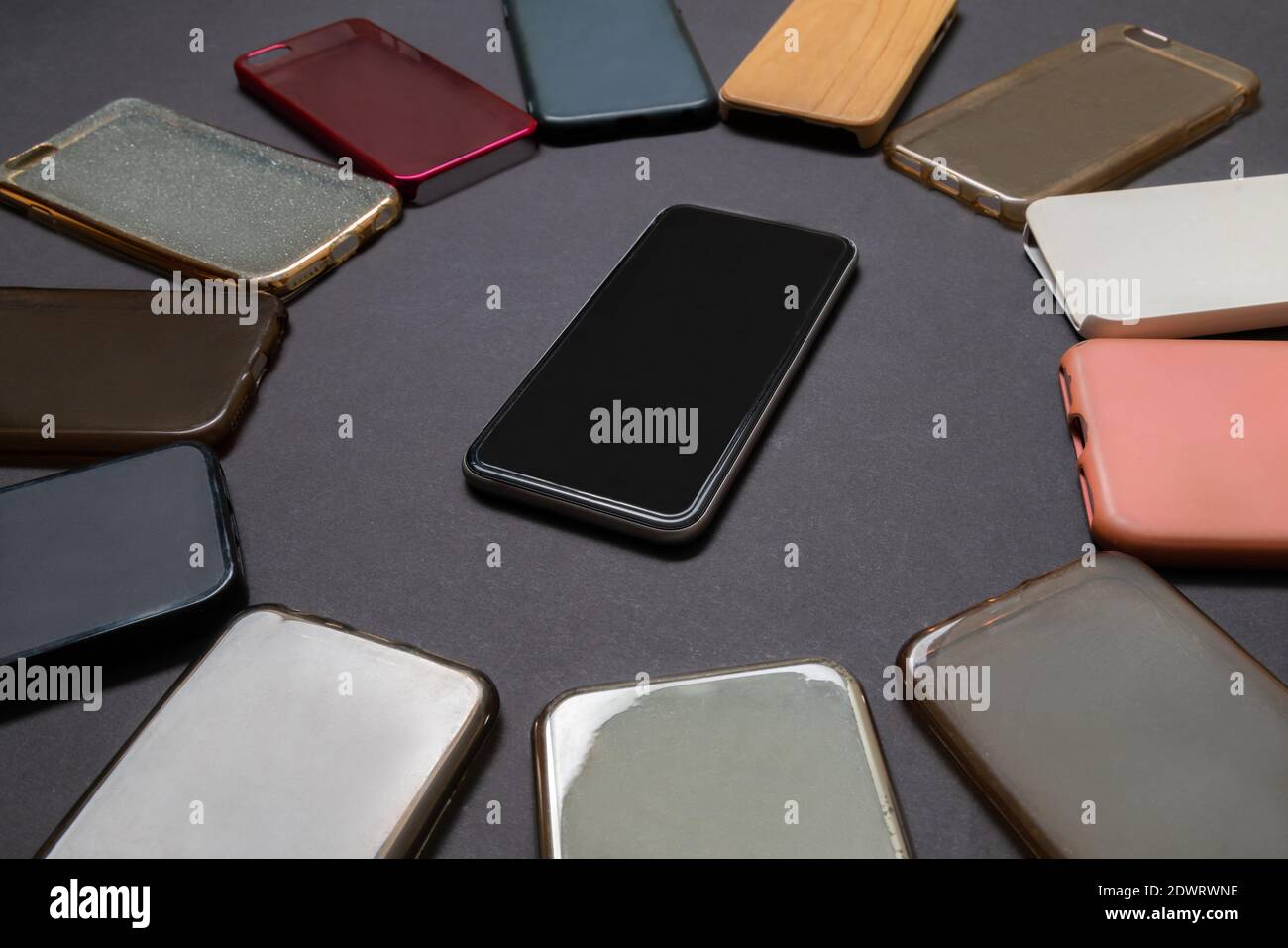 Pila di plastica multicolore torna copertine per i telefoni cellulari su sfondo nero con un telefono sul lato Foto Stock