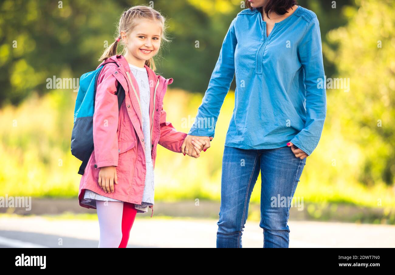 Madre che conduce la figlia a scuola su sfondo soleggiato natura Foto Stock