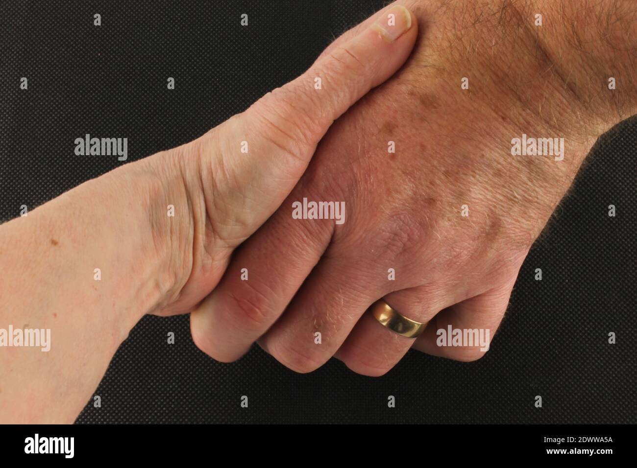 primo piano di un marito che tiene la mano di sua moglie su sfondo nero, aiutando il concetto di mano Foto Stock