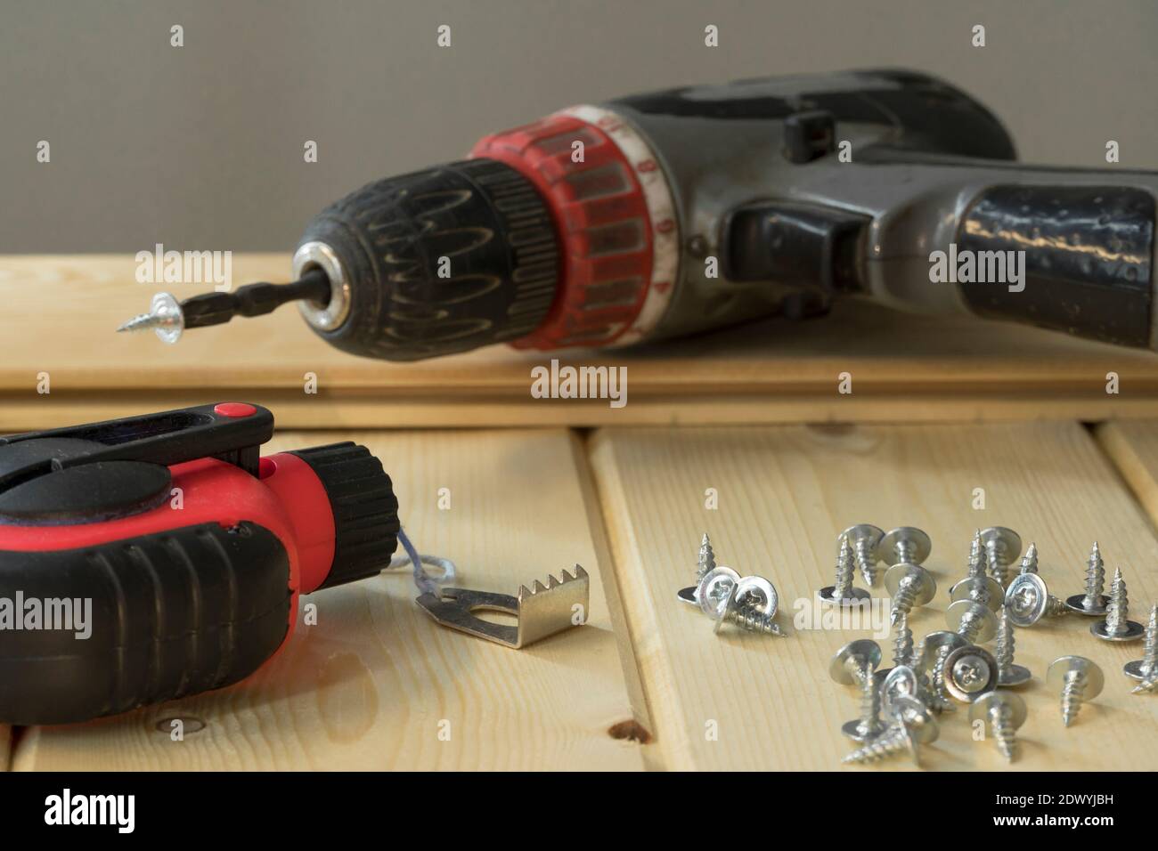 Trapano a batteria e viti. Trapano elettrico con punte da trapano, viti su fondo di legno. Mazzo di viti su tavole di legno. Strumenti assortiti. Profe di handyman Foto Stock